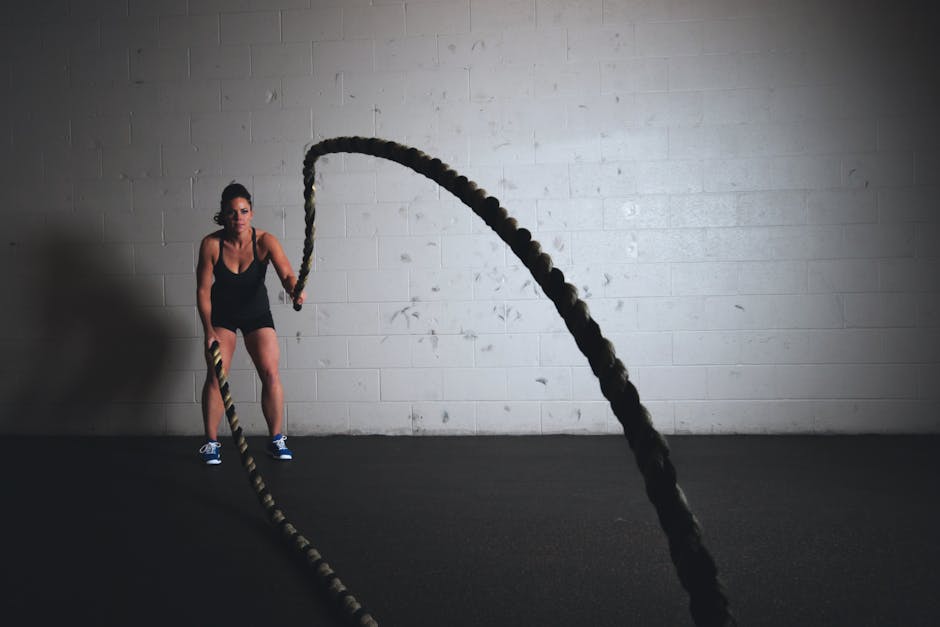 A focused woman performs a dynamic battle rope exercise in a gym setting, demonstrating strength and fitness
